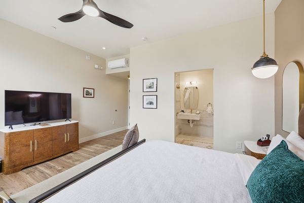 Bright bedroom showcasing the large fan, entry to bathroom, flat screen smart tv, and historical photos of Morro Bay.